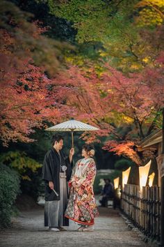 a man and woman standing under an umbrella in front of some trees with red leaves