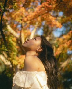 a woman standing in front of a tree with her head tilted to the side looking up