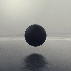 a black and white photo of a ball floating in the water on a foggy day