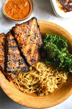 a plate with noodles, broccoli and some meat on it next to sauces