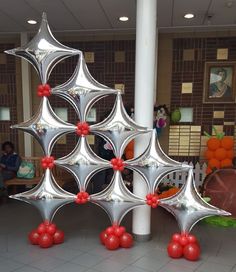 a large metal christmas tree with red balls on it's sides and people sitting in the background