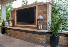 a television mounted to the side of a brick wall next to plants and potted plants