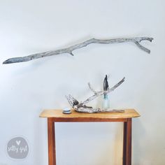 a wooden table topped with two vases and a branch mounted on the wall behind it