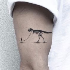 a person with a small tattoo on their arm holding a string attached to a dinosaur