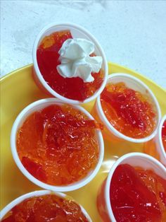 four small cups filled with jelly on top of a yellow plate and topped with whipped cream