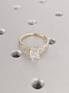 a gold ring with a princess cut diamond surrounded by small white dots on a gray surface