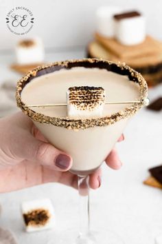 a hand holding a drink with marshmallows on the rim