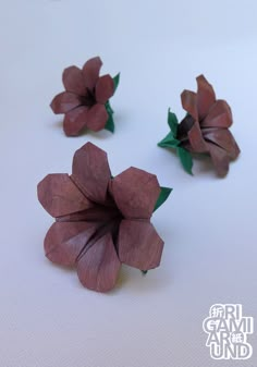 three paper flowers sitting on top of a white table next to each other with green leaves