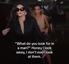 a woman in sunglasses walking down a street next to another person with a quote on it