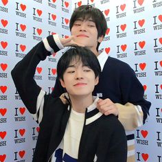 two young men standing next to each other in front of a wall with i love wish written on it