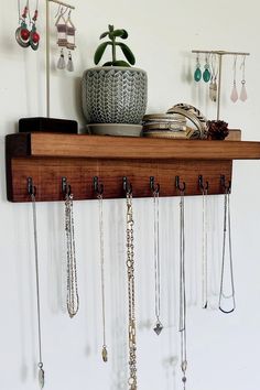 a wooden shelf with many necklaces hanging from it's sides and a potted plant in the background