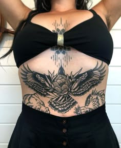 a woman with an eagle tattoo on her stomach is standing in front of a white wall