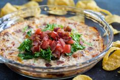 a glass bowl filled with food next to chips