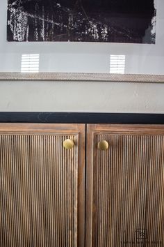 a wooden cabinet with two brass handles in front of a black and white painting on the wall