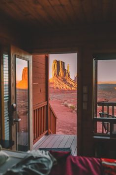 an open door leading to a balcony with mountains in the background and red dirt on the ground