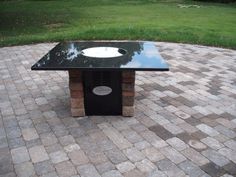 a black table sitting on top of a brick patio next to a green field with trees