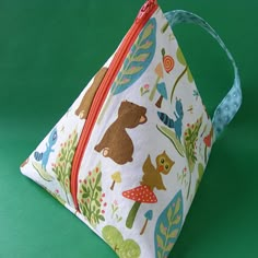 a small bag with animals on it sitting on a green surface, next to a red zipper