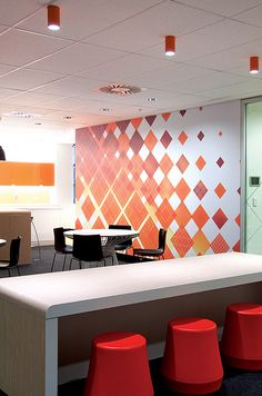 an office with orange and white decor on the walls, desks and stools