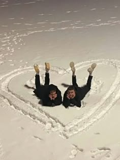 two people laying in the snow making a heart shape