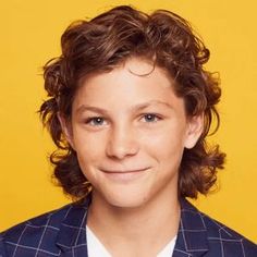 a young man with curly hair wearing a blue jacket and white shirt smiling at the camera