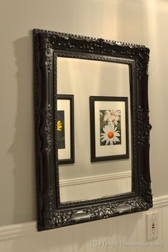 a mirror hanging on the wall above a sink in a room with white walls and black trim