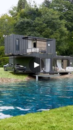 a house made out of shipping containers sitting on the side of a body of water