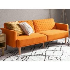 an orange couch sitting on top of a white rug next to a wooden end table