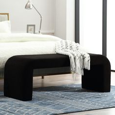 a black bench sitting on top of a blue rug next to a white bed in a bedroom