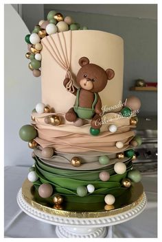 a three tiered cake with a teddy bear on it's top and balloons around the bottom