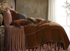 a bed with a brown bedspread and pillows on it in front of a window