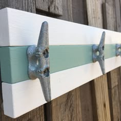 two metal hooks are attached to the side of a wooden fence with white and blue paint