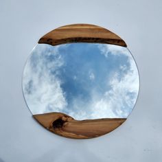 a circular mirror reflecting the sky and clouds on a white surface with wooden planks