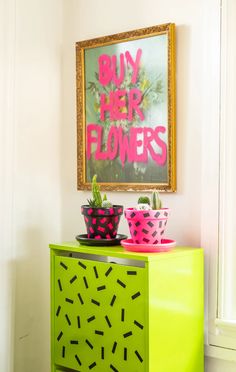 a green cabinet with pink and black flower pots on it in front of a painting