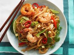 a white bowl filled with noodles and shrimp next to chopsticks on a table