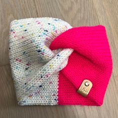 a pink and white knitted beanie with a gold pin on it's side