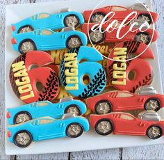 decorated cookies in the shape of race cars are on a white platter with red, blue and yellow frosting