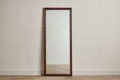 a mirror sitting on top of a wooden floor next to a white wall with a brown frame