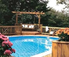 a backyard with a swimming pool and wooden decking, surrounded by flowering bushes and trees