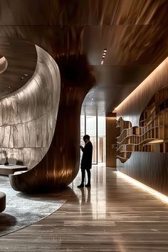 a man standing in the middle of a room next to a tall wooden sculpture and bookshelves