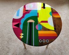 a round table with an abstract design on it's top and legs in front of a carpeted floor