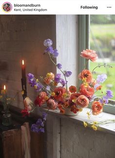 a window sill filled with flowers next to a lit candle