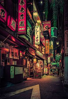 an alley way with neon signs on the buildings and trees in the city at night