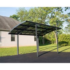 a metal carport in front of a house with grass and trees behind it on a sunny day