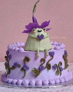 there is a cake decorated with purple frosting and flowers on the top, as well as an odd looking figure