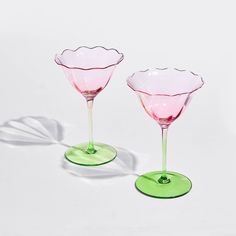 two pink and green wine goblets sitting side by side on a white surface