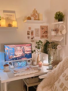 a white desk with a computer on top of it next to some plants and candles