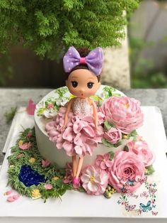 there is a cake decorated with flowers and a doll sitting on top of the cake