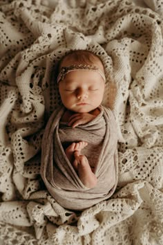 a newborn baby wrapped in a blanket on top of a white crocheted blanket