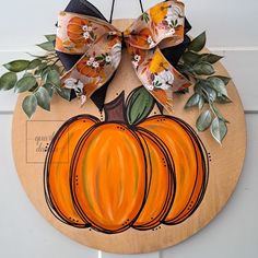 a wooden plaque with a pumpkin painted on it and a bow hanging from the front