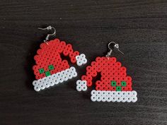 two red and white christmas themed earrings on a black surface, one with santa's hat